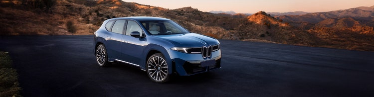 BMW iX3 front exterior on the road with view of the hills.