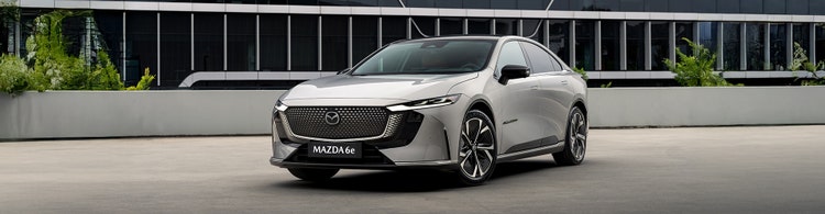 Mazda 6e front exterior view in front of a building. Novate a Mazda and contact Maxxia novated lease team today.