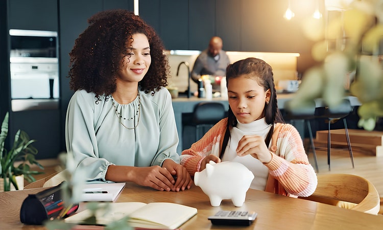 A mum guiding her daughter on saving her money with the piggy bank in the dining area.