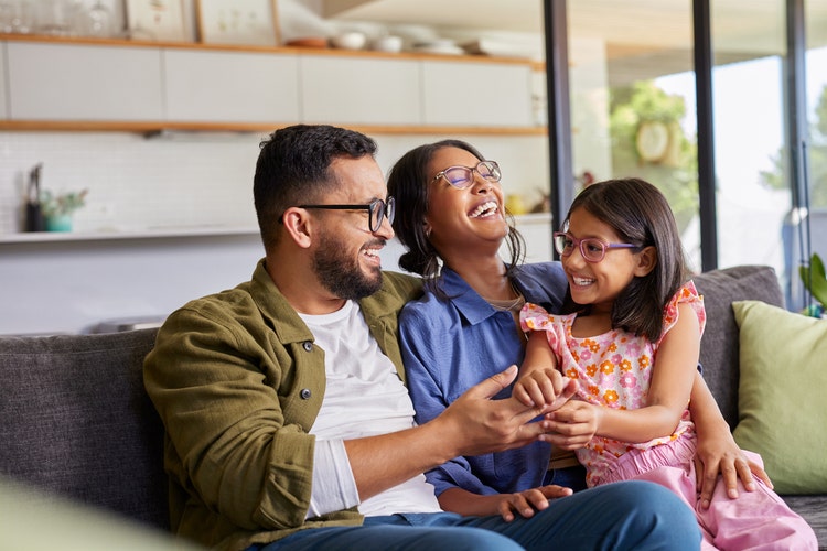A family smiling while sitting on their couch. How to reduce your taxable income and save on tax with salary packaging?