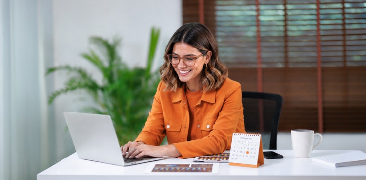 An employee smiling on her office desk starting a salary package with Maxxia before 1 April.
