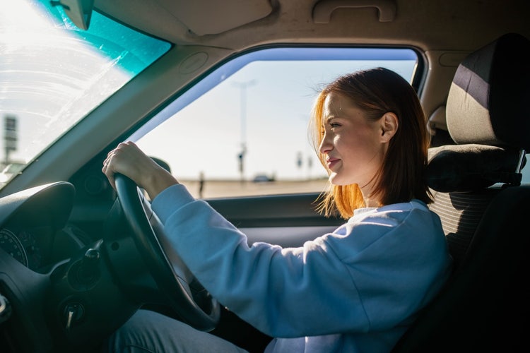 A woman smiling driving her new car. Discover how novated leasing on a brand new vehicle could offer valuable tax benefits.