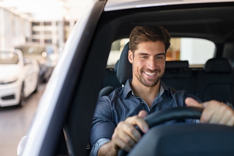 A man smiling while driving his car. Learn how you could get the usual tax benefits of novated leasing a second-hand vehicle.