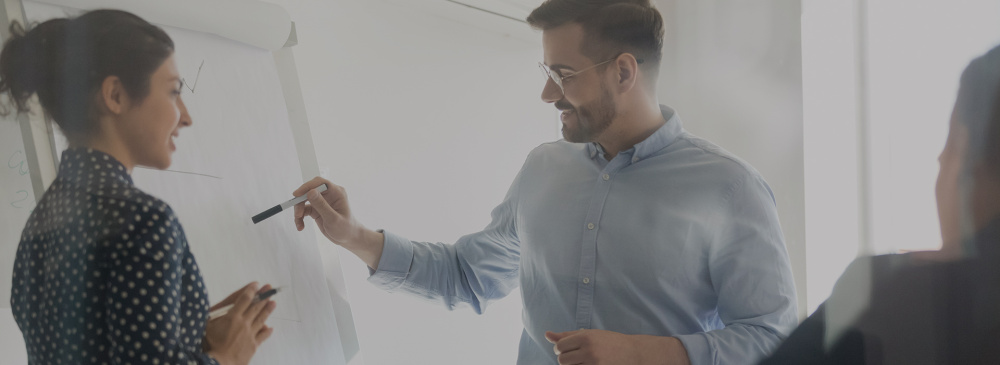 A man writing on a white board in front of his colleagues.