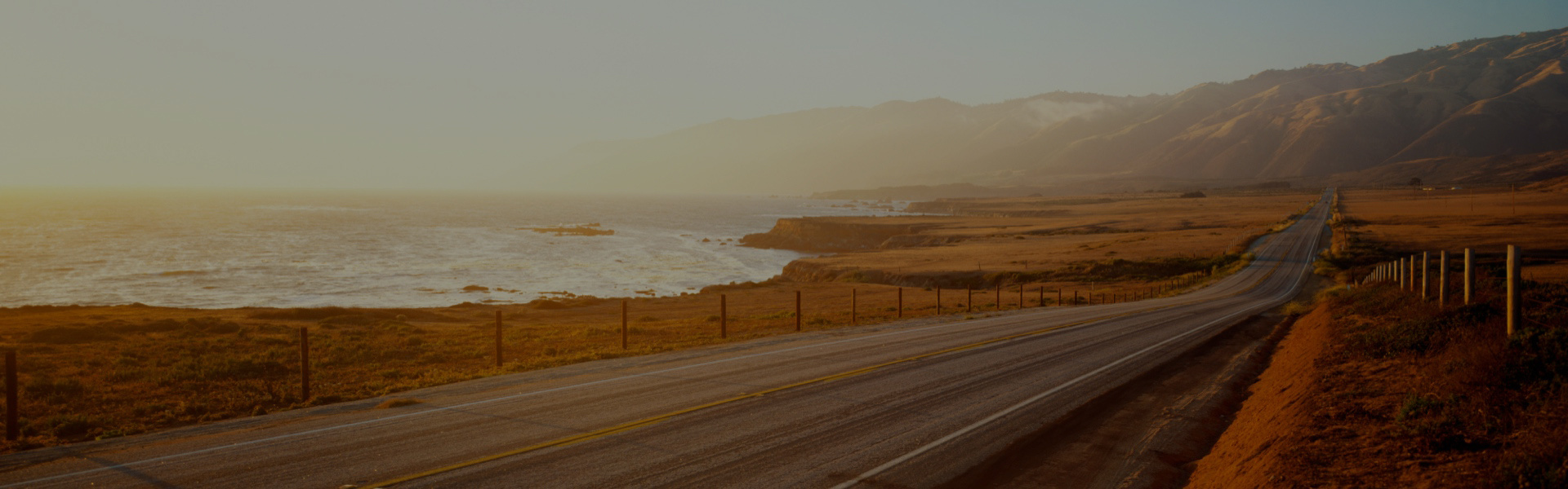 A long road along side the ocean during sunset.