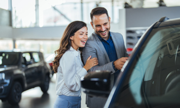 A man and a woman smiling looking at a car